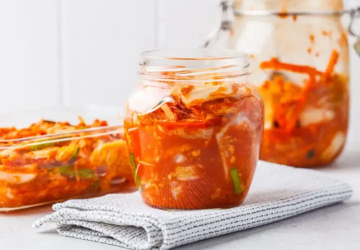 Słoiki i naczynie szklane wypełnione pikantnym, pomarańczowym kimchi.