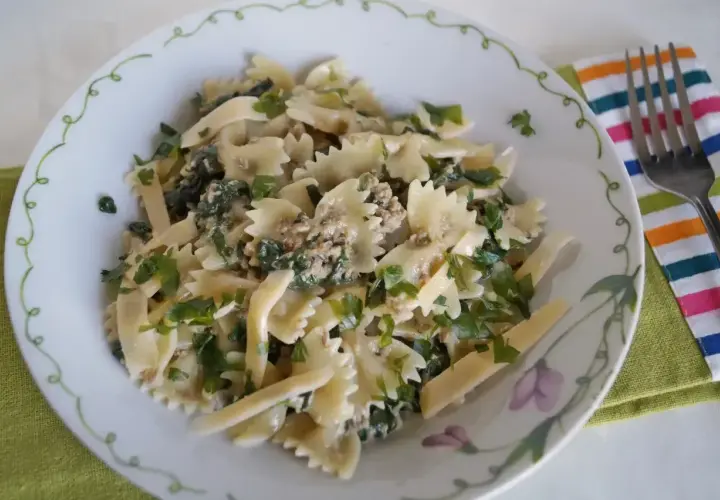 Pyszny makaron farfalle z tuńczykiem i szpinakiem, posypany świeżą natką pietruszki. Idealny na szybki obiad.