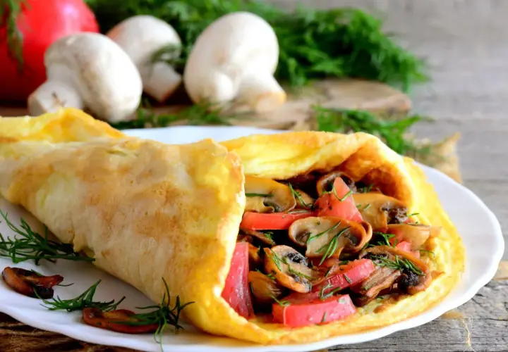 Puszysty omlet z pieczarkami i pomidorami, udekorowany koperkiem.