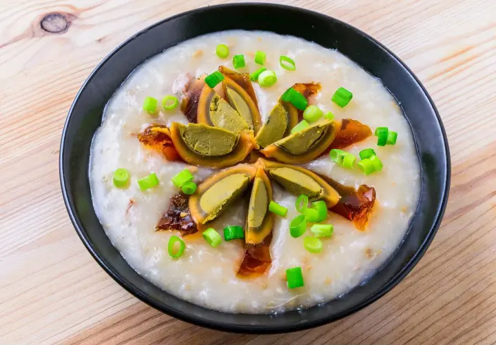 Miseczka z congee, ozdobiona połówkami jajka stuletniego, posypana szczypiorkiem i skropiona olejem chili.