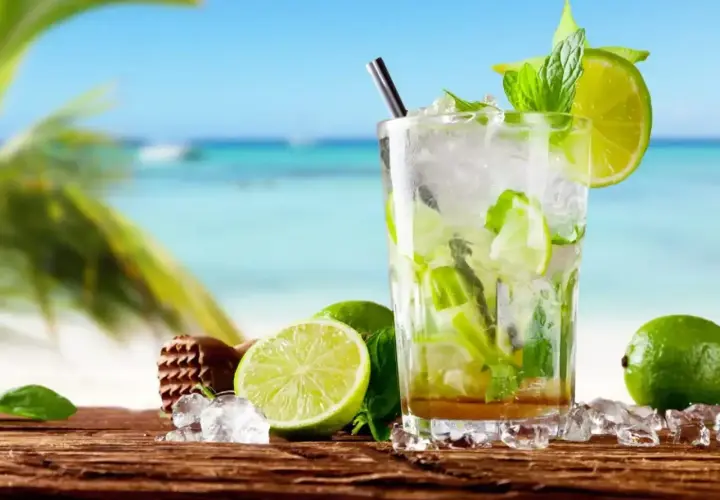Szklanka orzeźwiającego mojito z limonką i miętą na tle plaży.