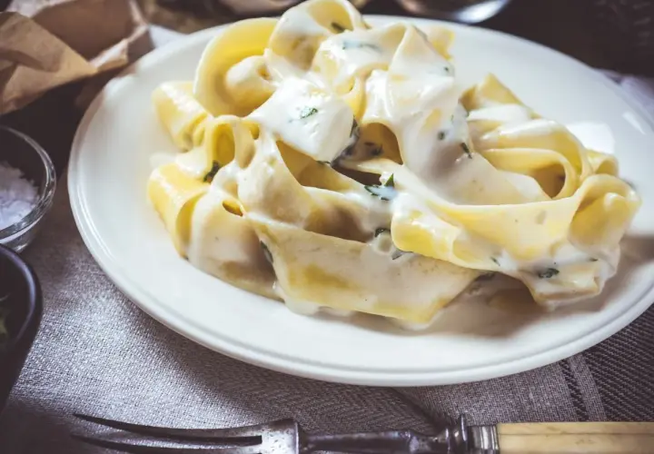 Makaron tagliatelle w kremowym sosie serowym z ziołami na białym talerzu.