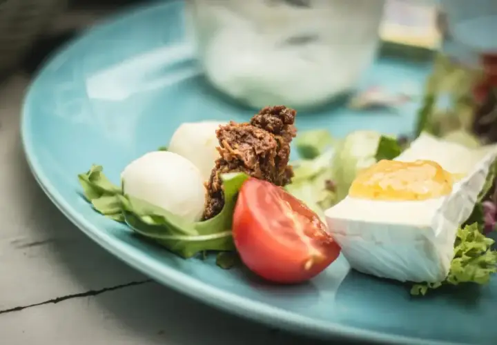 Keto śniadanie: ser brie z dżemem, kulki mozzarelli, pomidor i rukola na niebieskim talerzu.