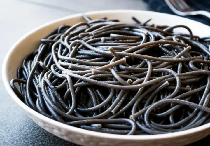 Czarny makaron spaghetti w białej misce, zbliżenie.