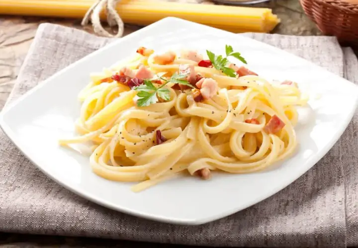 Talerz spaghetti carbonara z boczkiem i natką pietruszki, na lnianej serwetce.