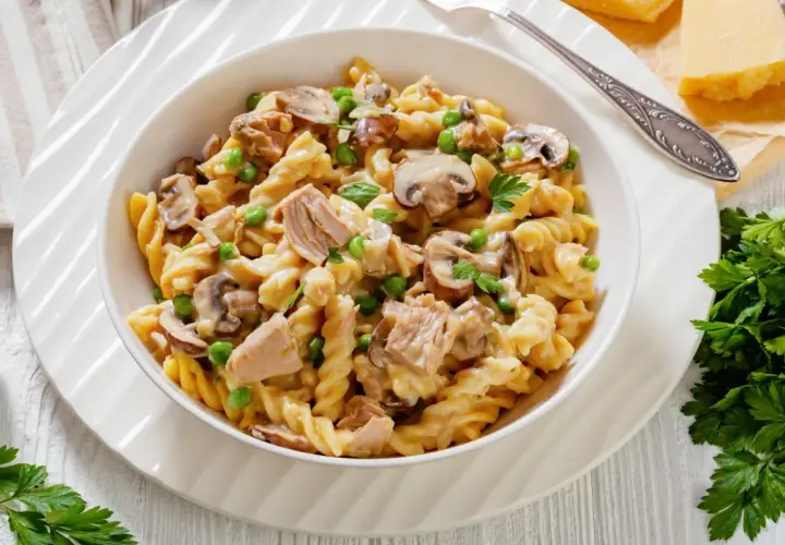 Makaron fusilli z tuńczykiem, groszkiem i pieczarkami w kremowym sosie, udekorowany natką pietruszki.