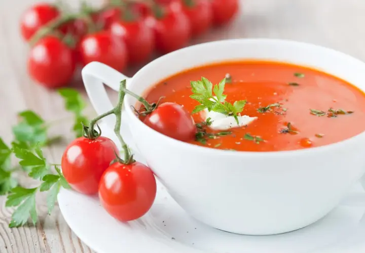 Zupa pomidorowa, ozdobiona gałązką pomidorków i natką pietruszki, wygląda apetycznie. Ile waży zupa pomidorowa? To zależy od porcji!