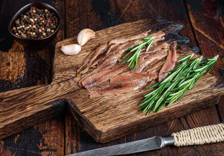 Filety anchois z rozmarynem i czosnkiem na drewnianej desce.