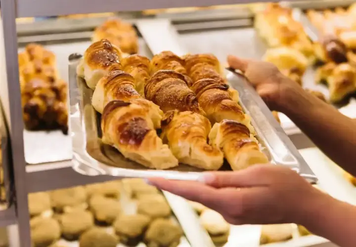 Taca z croissantami, którą trzymają ręce, na tle innych wypieków.