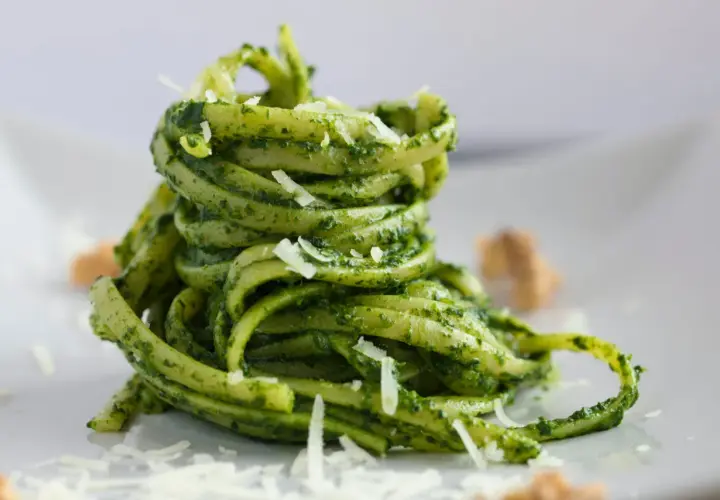 Makaron tagliatelle z zielonym pesto bazyliowym i startym parmezanem na białym talerzu.