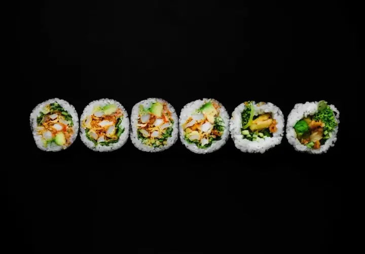 Sześć grubych rolek sushi futomaki z widocznym nadzieniem na czarnym tle.