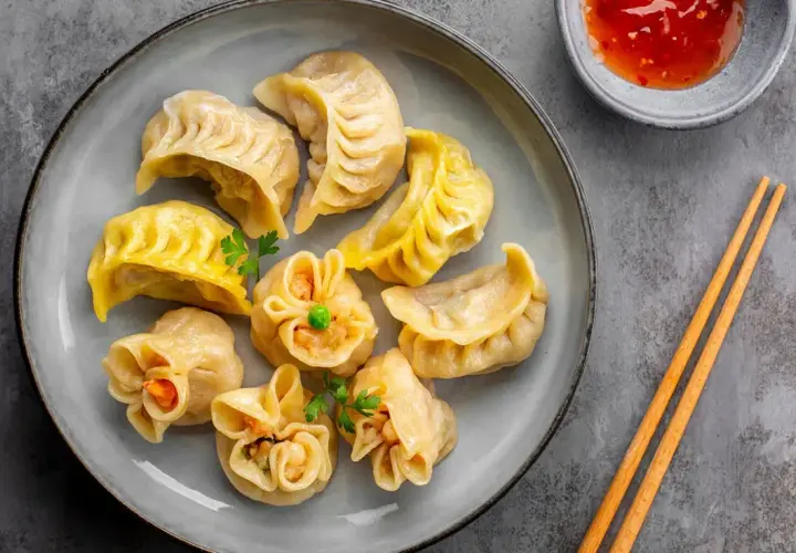 Talerz pełen różnorodnych pierożków dim sum, z sosem i pałeczkami. Idealna przekąska.