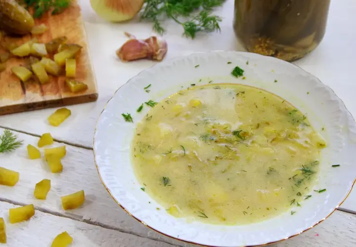 Talerz zupy ogórkowej, obok deska z ogórkami, koperek i cebula.