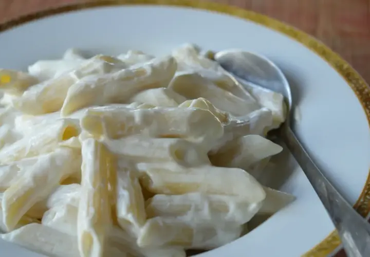 Makaron penne w kremowym sosie z twarogu na talerzu ze srebrną łyżką.