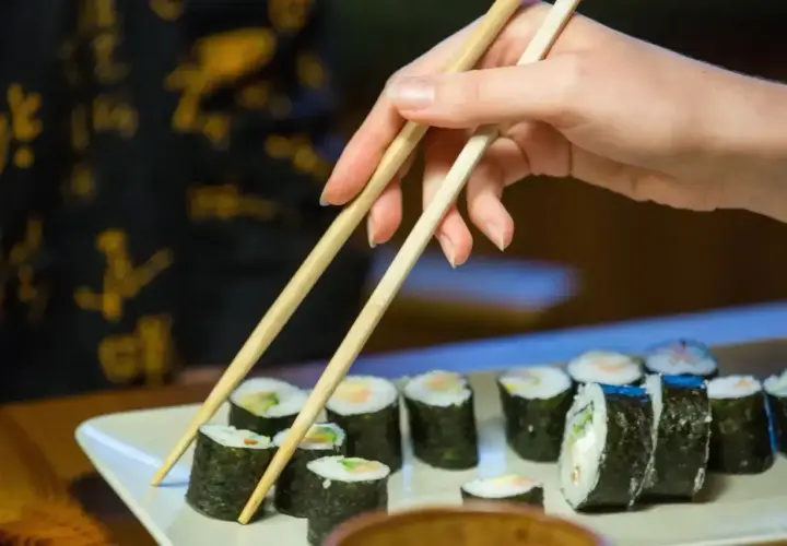Dłoń z pałeczkami sięga po rolkę sushi. Smaczne i zdrowe, ale warto pamiętać o sushi kcal.