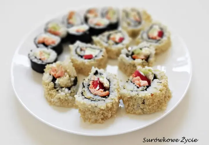 Talerz z rolkami sushi uramaki z ryżem na zewnątrz, posypanymi sezamem, z łososiem i warzywami.