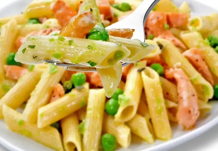 Makaron penne z łososiem i groszkiem w kremowym sosie na widelcu.