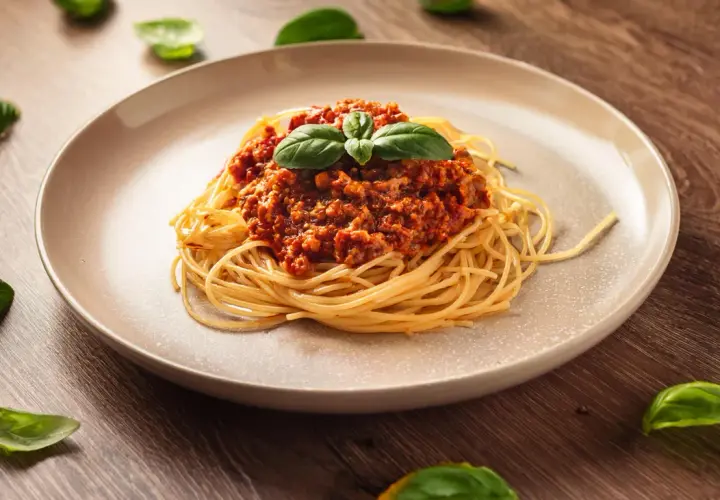Talerz spaghetti z sosem bolońskim i listkami bazylii na drewnianym tle.