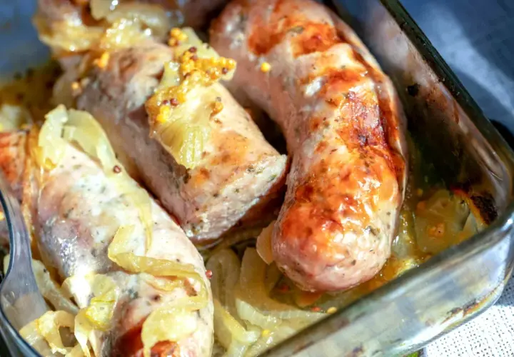 Soczysta biała kiełbasa pieczona w cebuli i musztardzie, podana w szklanym naczyniu.