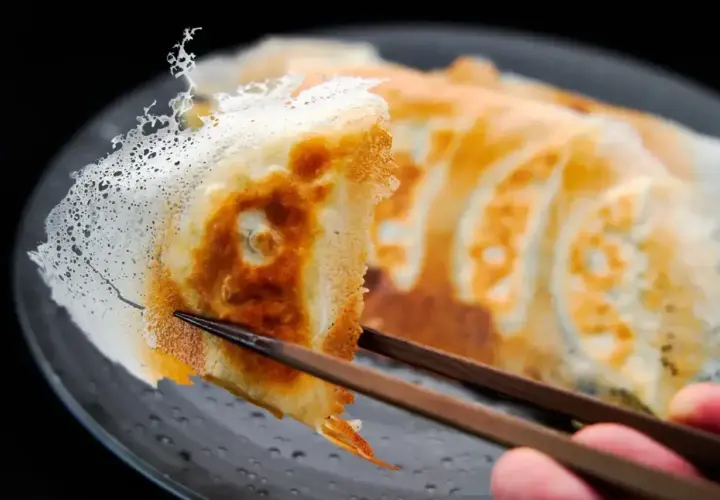 Chrupiące pierożki gyoza z delikatną, koronkową skórką, podniesione pałeczkami.