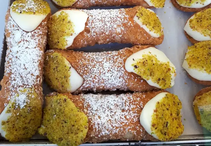 Zbliżenie na sycylijskie cannoli posypane cukrem pudrem i pistacjami, z kremowym nadzieniem.