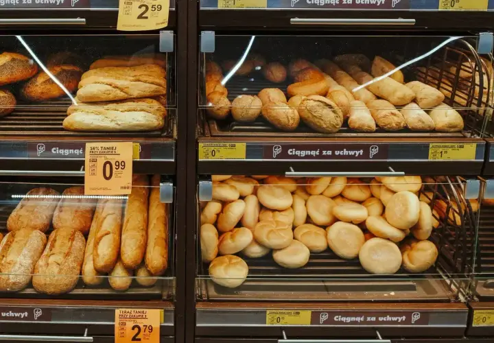 Różnorodne pieczywo, w tym bagietki i bułki, na półkach sklepowych. Widać promocje na chleb ig.