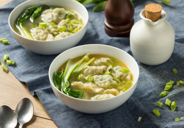Dwie miseczki aromatycznej zupy won ton z pierożkami, zielonymi warzywami i szczypiorkiem, gotowe do podania.