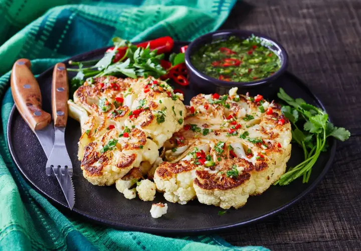 Idealny pomysł na kalafiora na obiad: pieczone steki z kalafiora z sosem chimichurri, posypane chili i pietruszką.