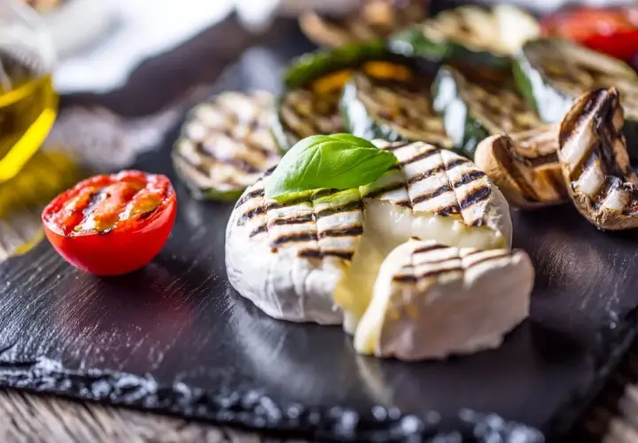Kremowy camembert z grilla z pomidorkiem i warzywami na czarnej desce.