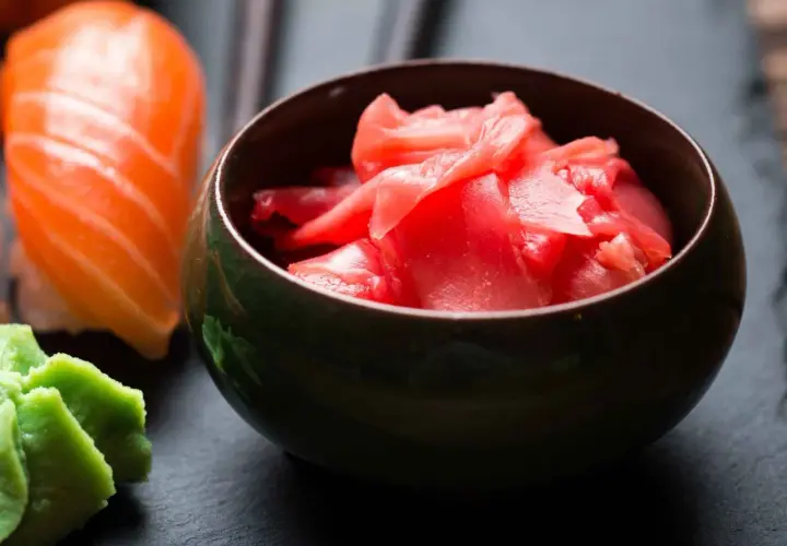 Miseczka z różowym, marynowanym imbirem obok sushi i wasabi. Idealny dodatek do japońskich przysmaków.