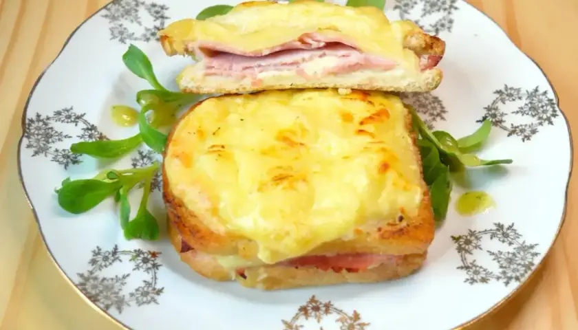 Dwie francuskie kanapki croque monsieur z serem i szynką, podane na talerzu z sałatką.