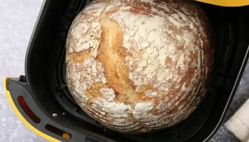 Złocisty bochenek chleba w czarnej frytkownicy beztłuszczowej z żółtymi akcentami.