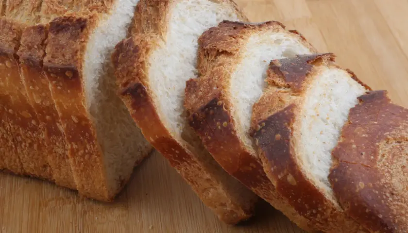 Pokrojony bochenek chleba z chrupiącą skórką na drewnianej desce.