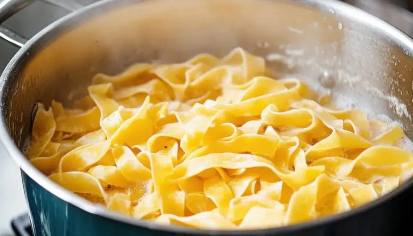 Szeroki makaron tagliatelle gotuje się w garnku z bulgoczącą wodą.