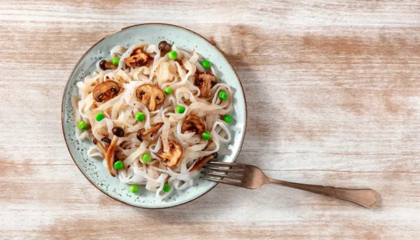 Makaron konjac z pieczarkami i groszkiem na talerzu, obok widelec.
