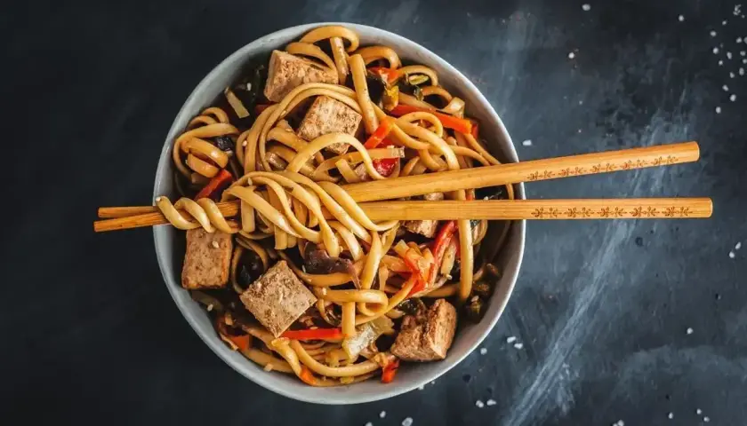 Miska domowego udonu z tofu i warzywami, podana z pałeczkami.