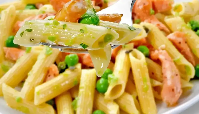 Makaron penne z łososiem i groszkiem w kremowym sosie na widelcu.