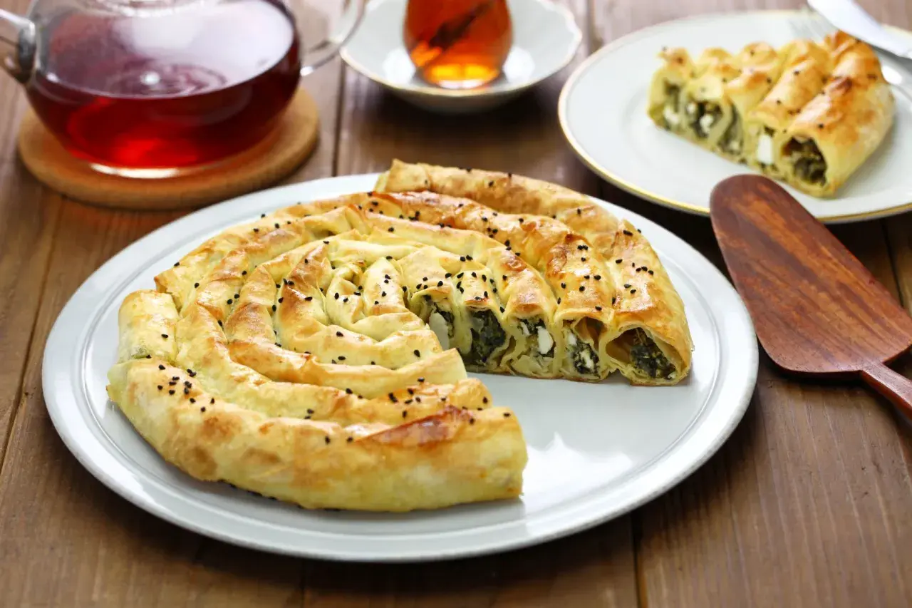 Chrupiący borek ze szpinakiem i serem na talerzu, obok filiżanka herbaty.