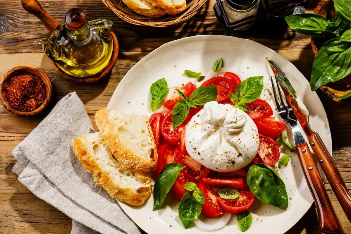 Burrata z pomidorami, bazylią i pieczywem na talerzu.