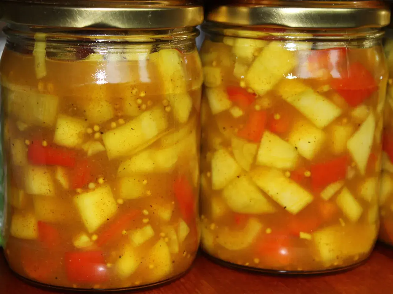 Dwa słoiki z marynowaną cukinią w zalewie curry z kawałkami papryki i gorczycą.