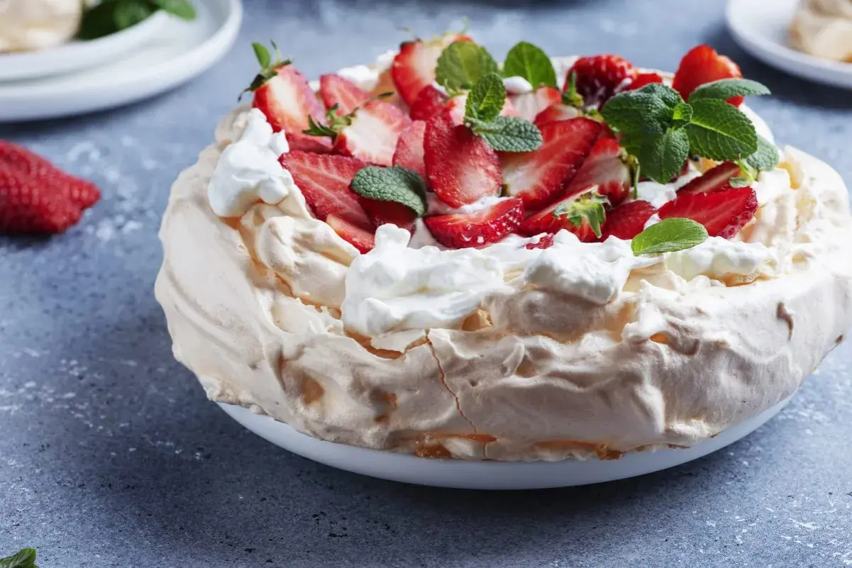 Beza z mascarpone i truskawkami, ozdobiona miętą.