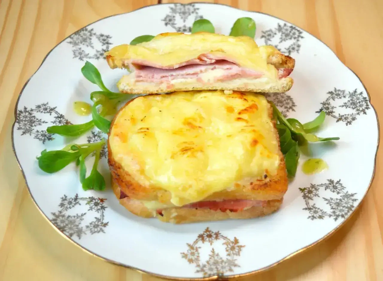 Dwie francuskie kanapki croque monsieur z serem i szynką, podane na talerzu z sałatką.