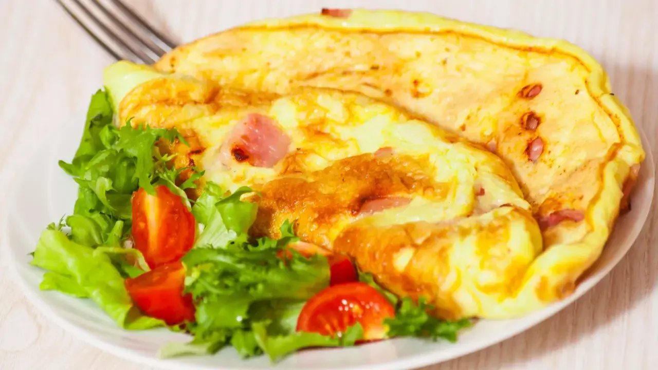 Złocisty omlet z szynką i pomidorkami koktajlowymi na talerzu z sałatą.