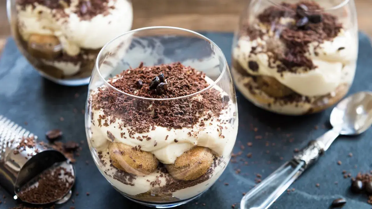Deser tiramisu w szklance, posypany startą czekoladą i ziarnami kawy.