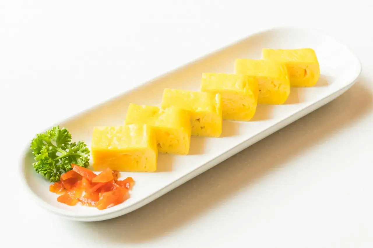 Japoński omlet tamagoyaki pokrojony w plastry, podany z natką pietruszki i marynowaną marchewką.