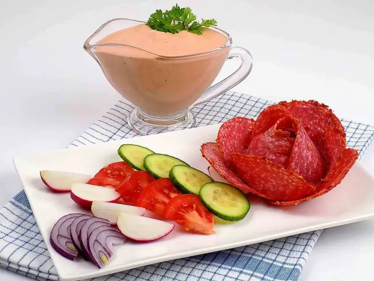 Sos do kebaba w sosjerce, obok talerz z warzywami i róża z salami.