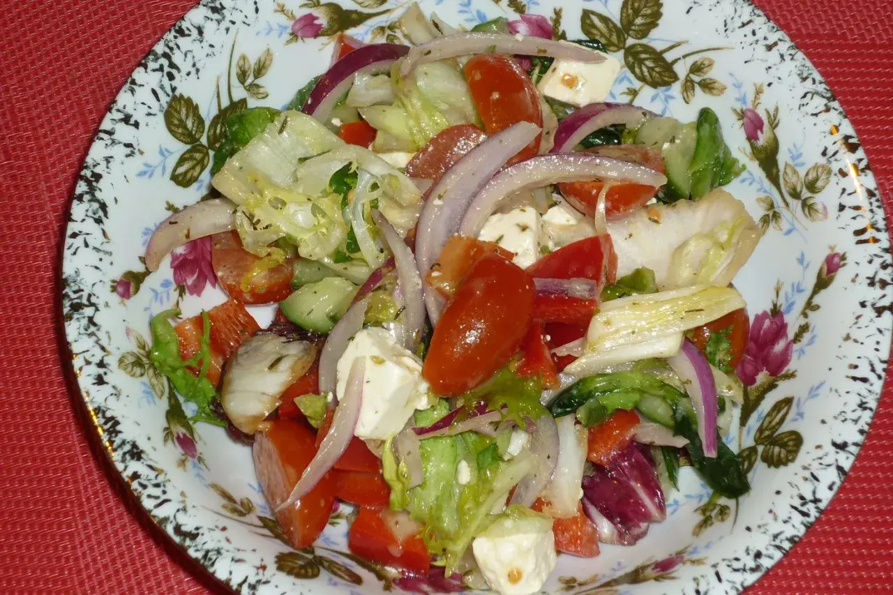 Kolorowa sałatka z mixu sałat, pomidorów, ogórka, sera feta i czerwonej cebuli na ozdobnym talerzu.