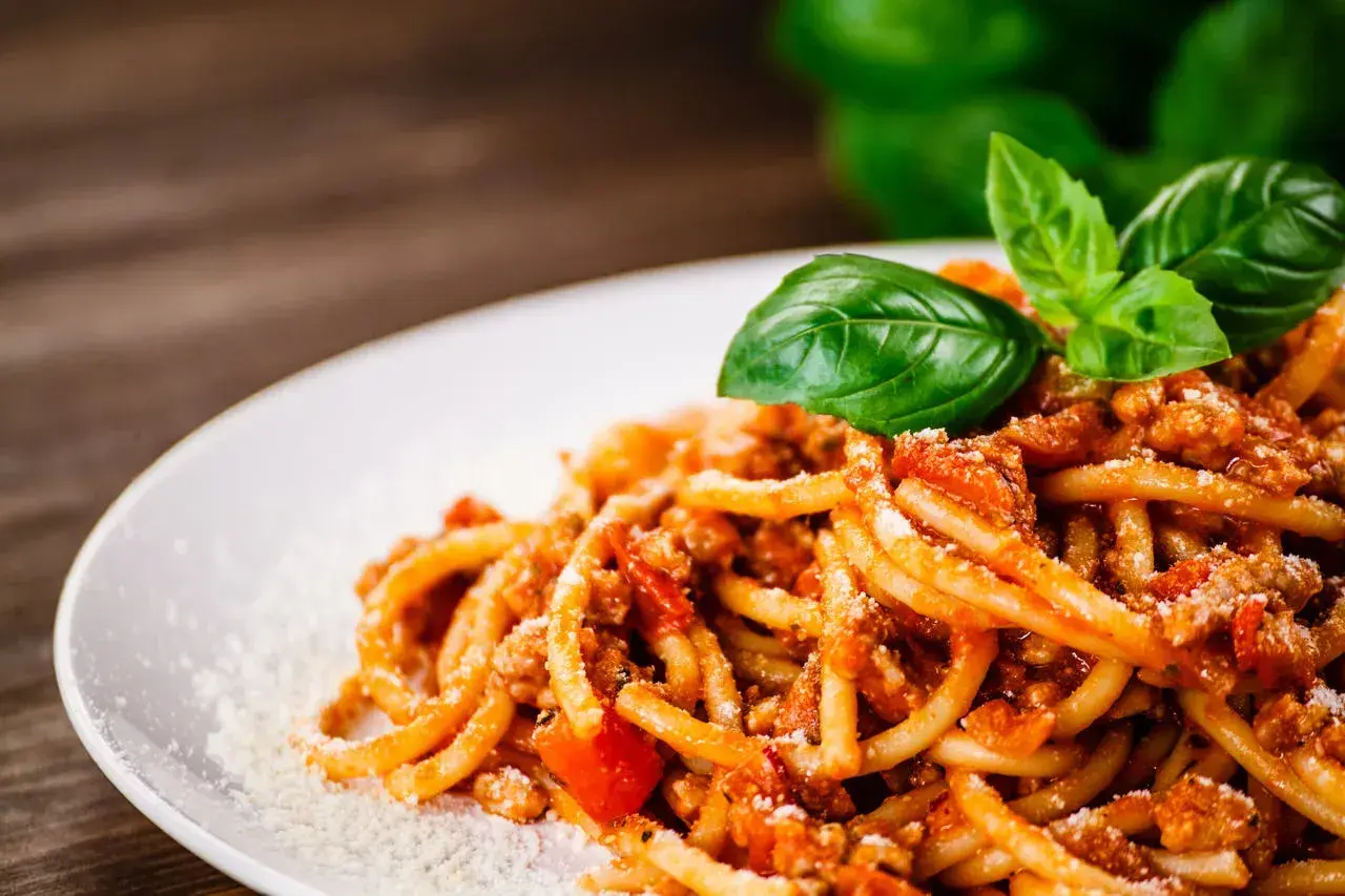 Talerz spaghetti z ragù mięsnym, posypany parmezanem i udekorowany listkami bazylii.