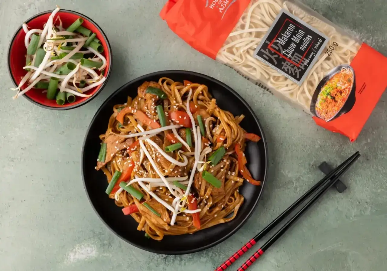 Talerz makaronu chow mein z warzywami i kiełkami fasoli, obok paczka makaronu i miseczka kiełków.