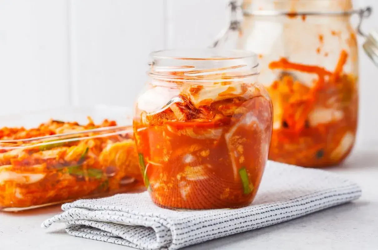 Słoiki i naczynie szklane wypełnione pikantnym, pomarańczowym kimchi.